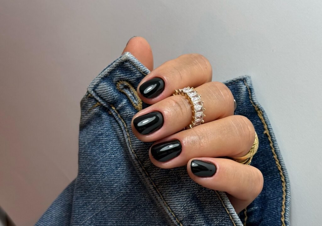 Ongles courts avec vernis noir brillant, main posée sur une veste en jean.