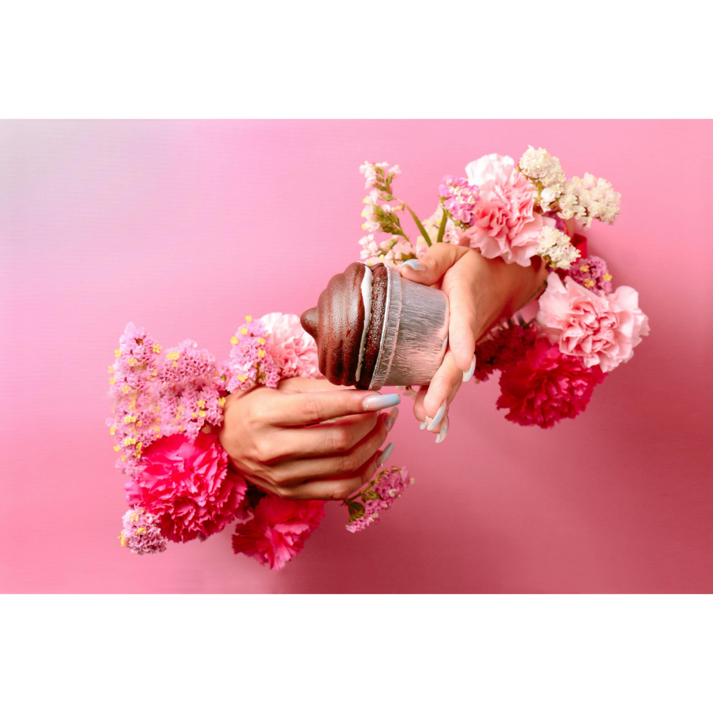 Manucure de printemps pastel avec ongles longs tenant un cupcake, entourée de fleurs roses.