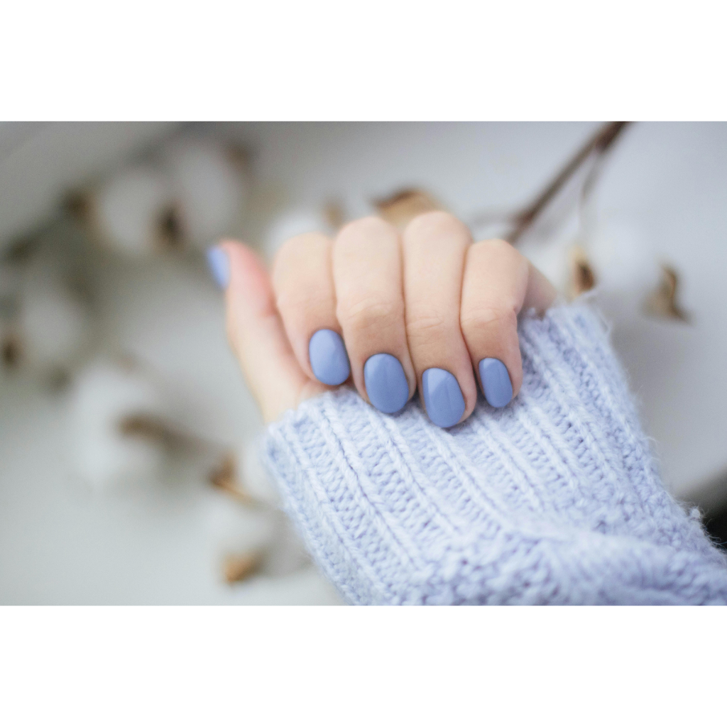 Ongles minimalistes en bleu mat, sur main posée avec pull en maille douce.