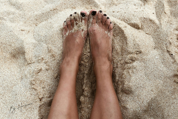 Pieds aux ongles soignés posés sur le sable, rappelant que l'été approche